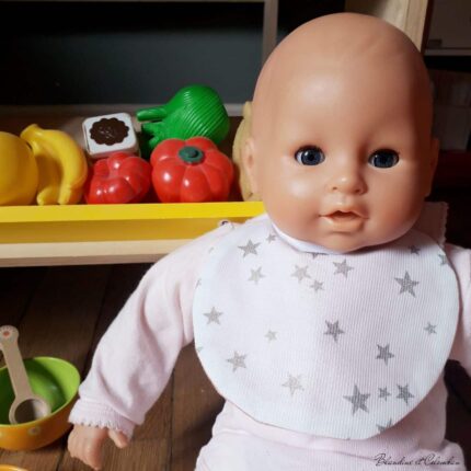 Bavoir de poupée, étoiles argentées sur fond blanc.